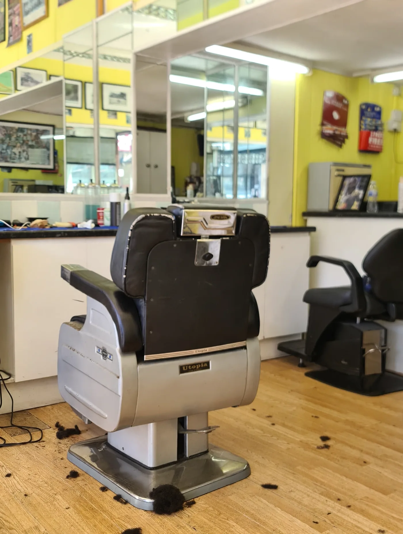 Inside 1st For Choice Barbers: a vintage Utopia barber chair in front of mirrors and yellow walls with framed pictures
