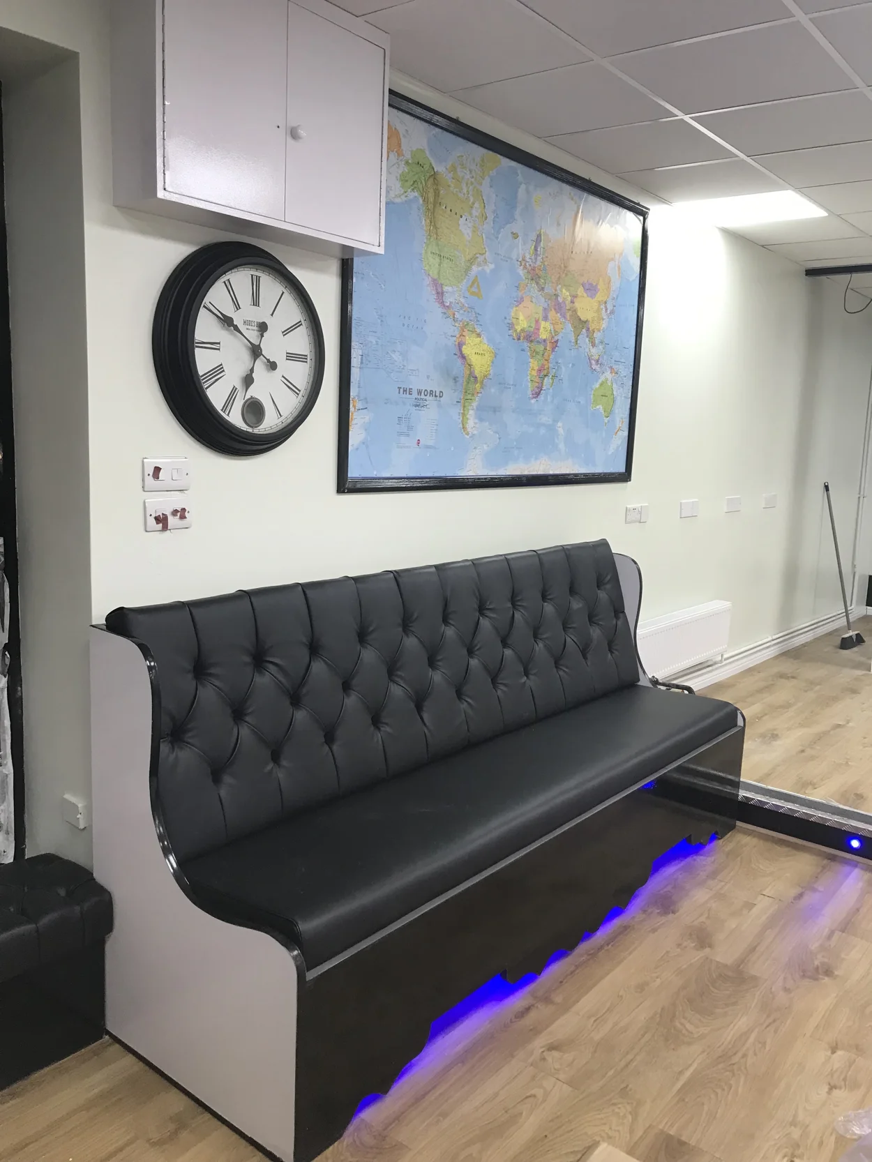 Inside A Star Barbershop — a black leather waiting bench under a big wall clock and a framed world map