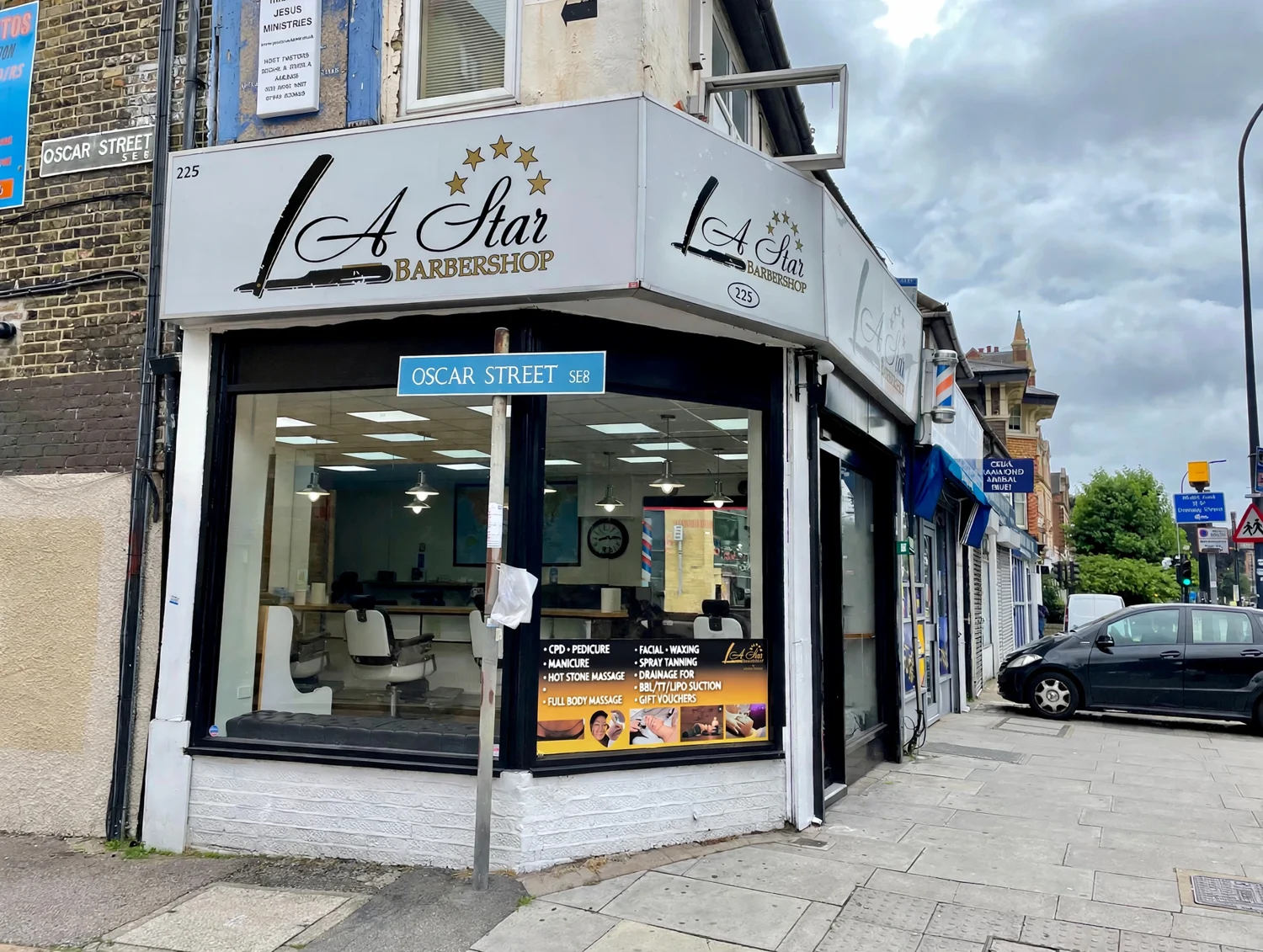 The A Star Barbershop corner shopfront on Lewisham Way — white fascia with script logo and gold stars, beside the Oscar Street sign