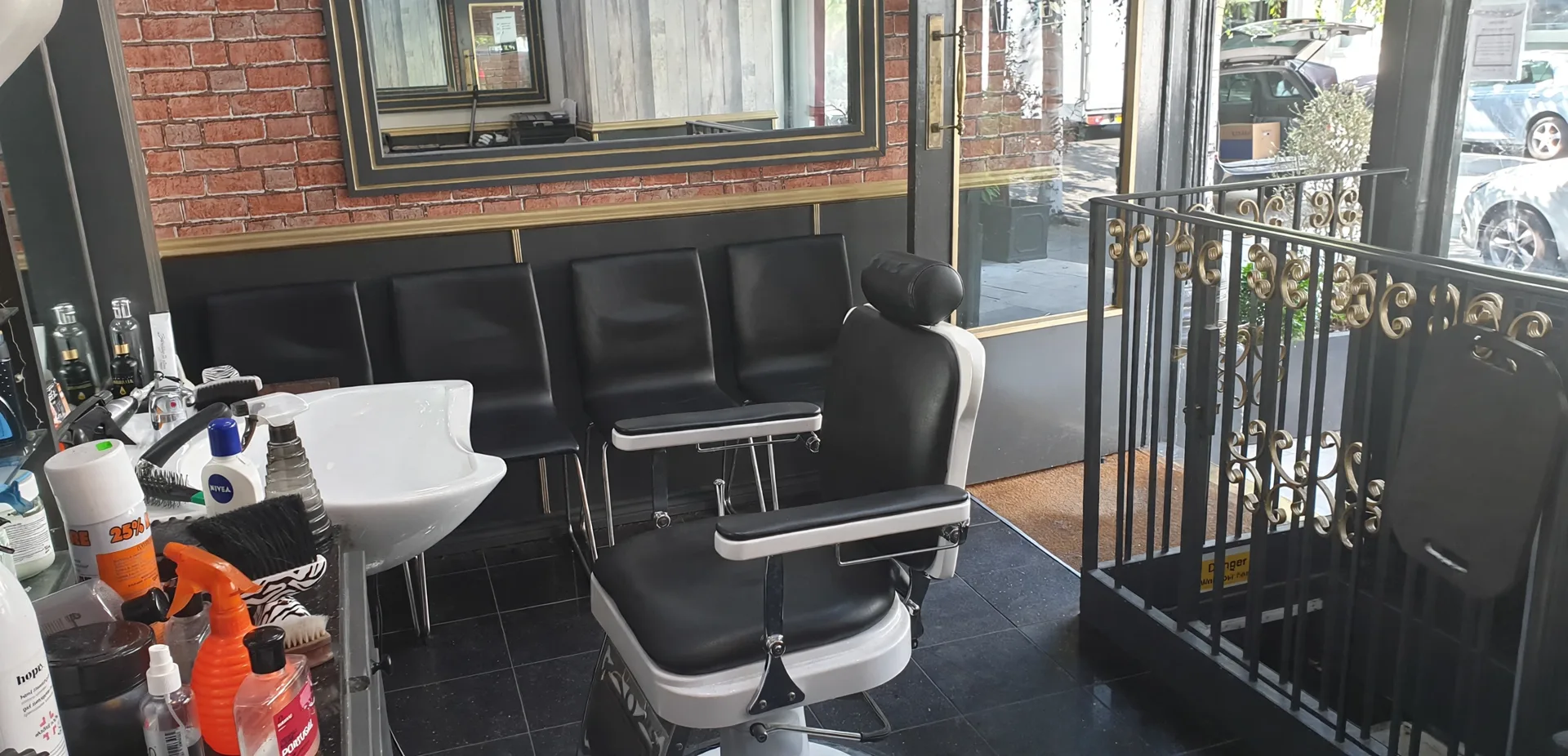 Inside Abbey Barbers: a black leather barber chair, white washbasin, waiting chairs against a red brick wall with brass trim and an ornate railing