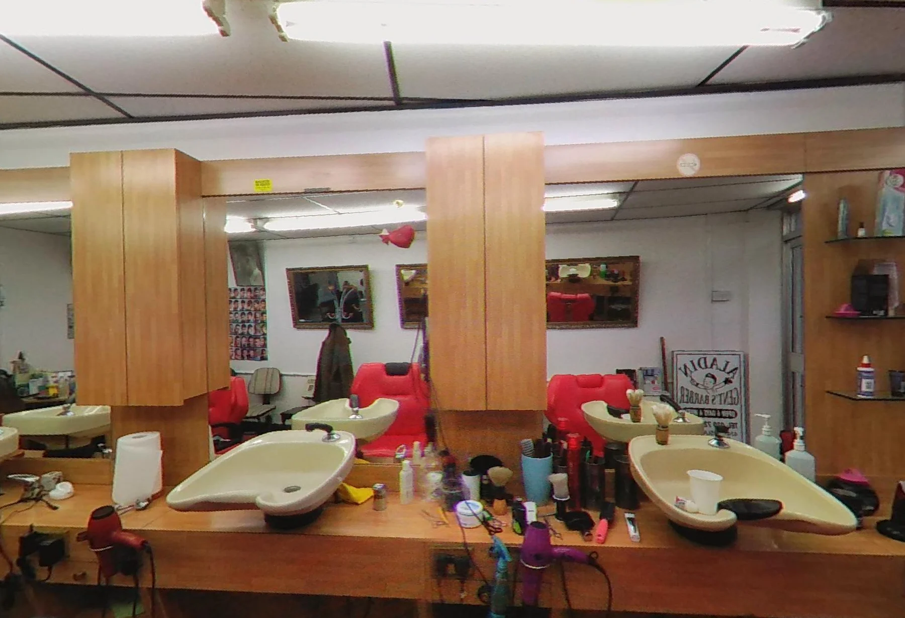 Inside Aladin Gent's Barber: the wooden counter with cream wash basins, big mirrors, tools laid out and red chairs reflected in the glass