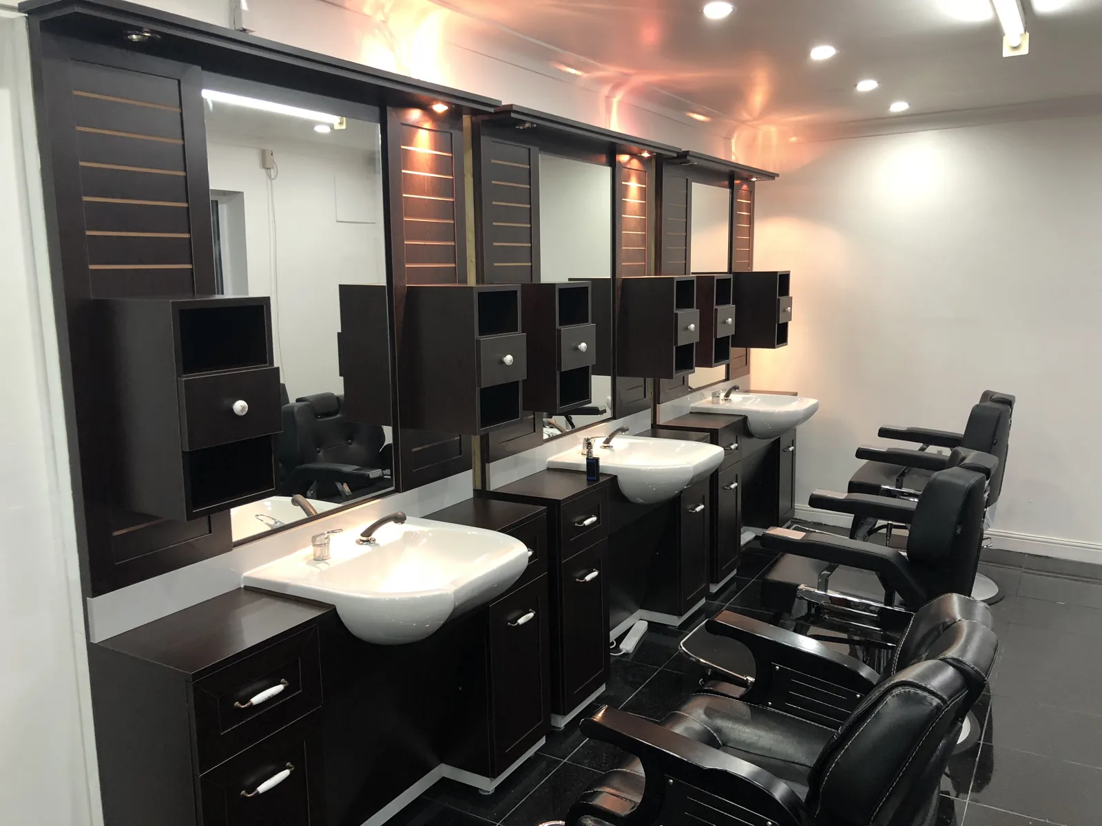 Inside Barber King: dark stained-wood barber stations with mirrors, white ceramic sinks, black leather chairs and warm amber lighting