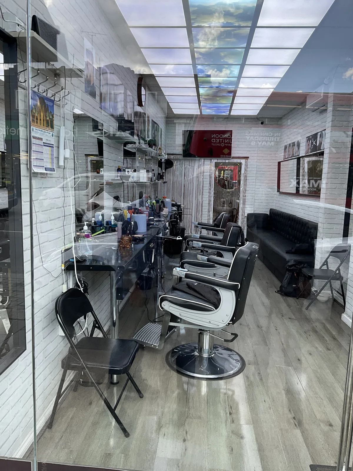 Inside Best Barbershop: white-brick walls, black barber chairs and mirrors under ceiling panels printed with sky and clouds