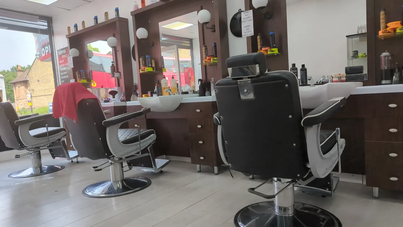 Inside Chopping Barbers: dark walnut mirror stations with white globe lights, white wash basins, black barber chairs and the shop's cash-only sign