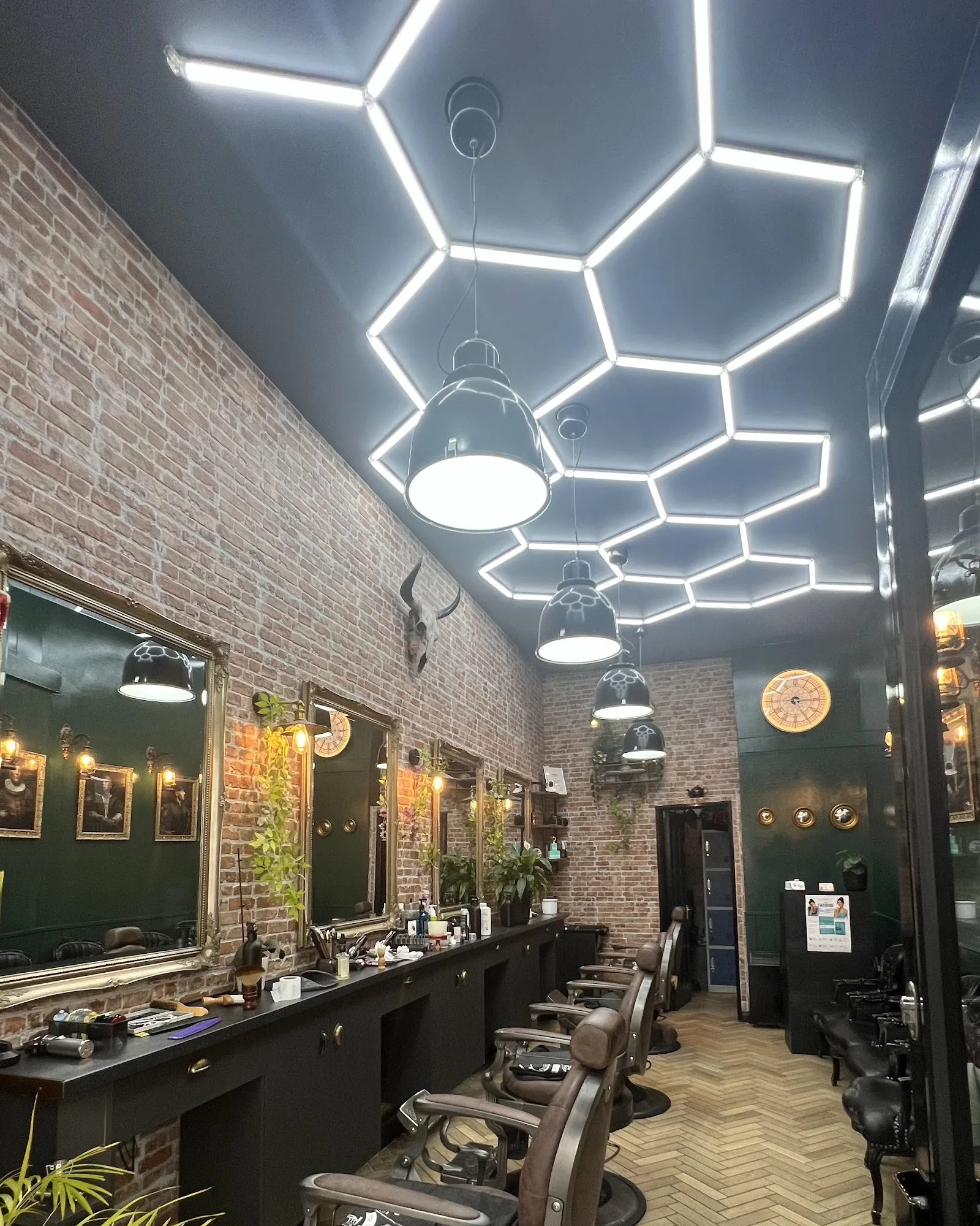 Inside Cut & Go: vintage leather barber chairs along a brick wall with brass mirrors, under a honeycomb LED ceiling