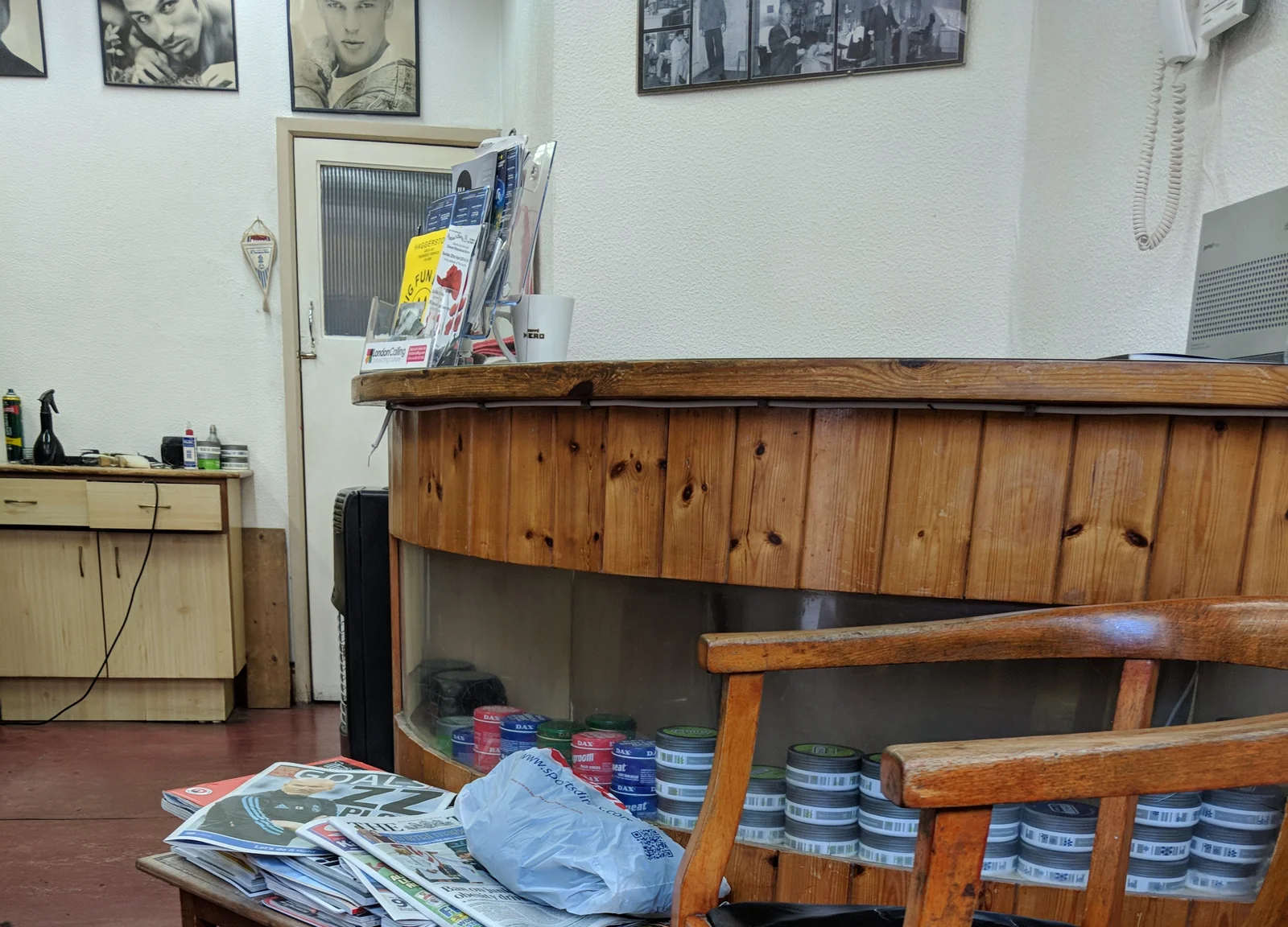 Inside Gino's: the curved pine counter with Dax wax tins in its glass case, wooden waiting chairs, a newspaper table and framed photos on the wall