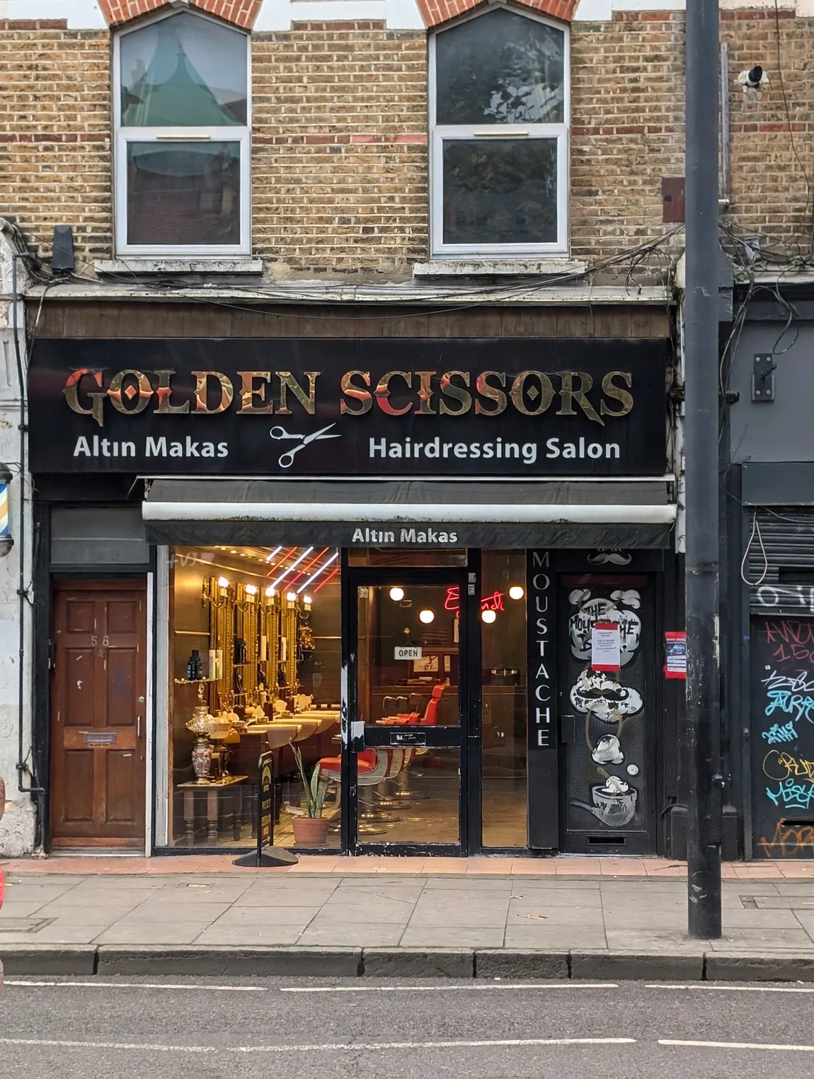 Golden Scissors on Stoke Newington Road: the black fascia with gold lettering, Altın Makas awning, moustache door artwork and the brown door of number 58