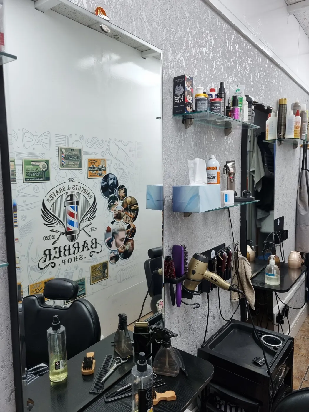 A barber station at HK Haircuts — mirror, tools and the shop's EST. 2020 mural