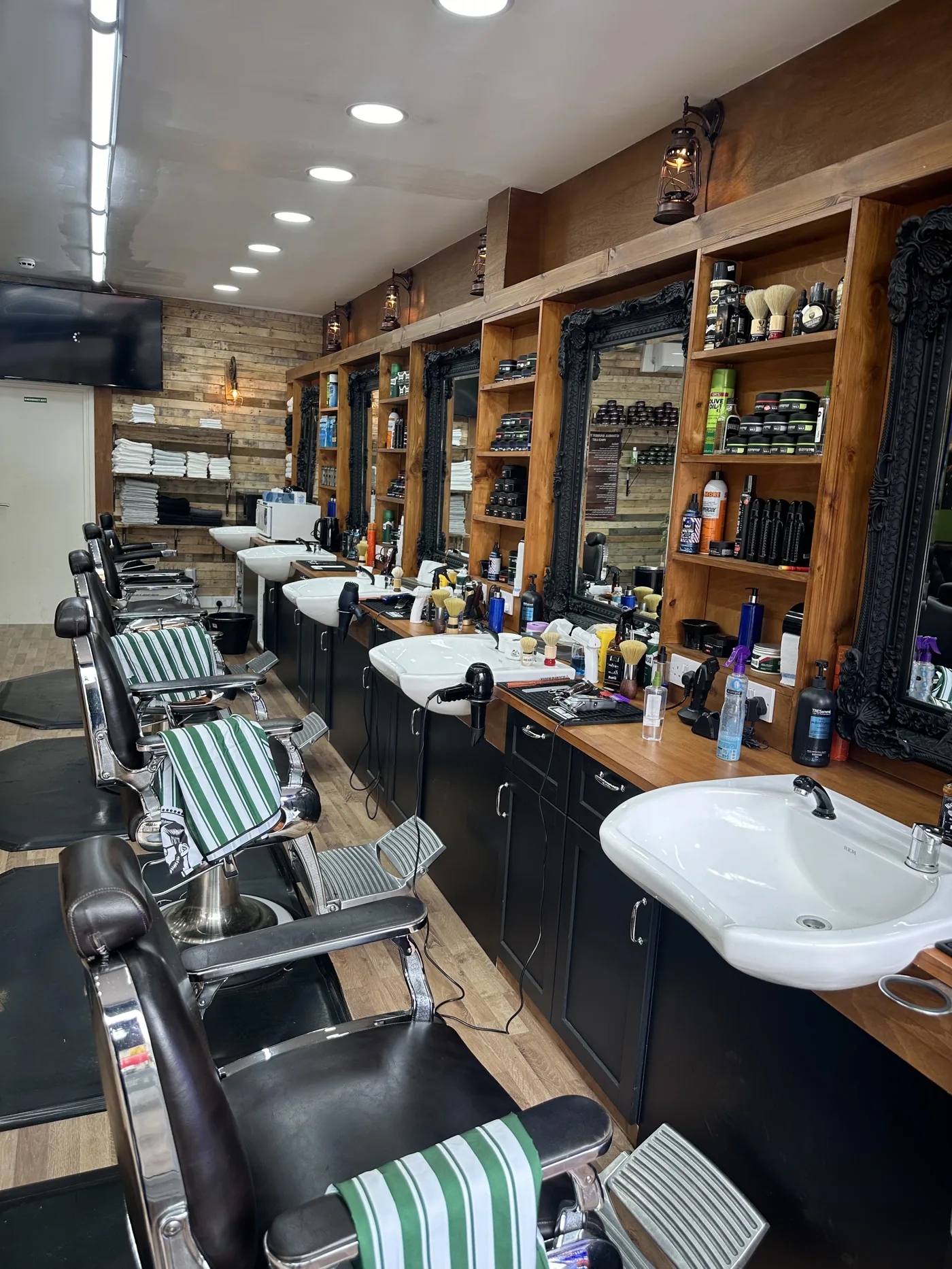 Inside Istanbul Barbers Tooting: a long timber-panelled salon with ornate mirrors, washbasins and barber chairs with green-striped towels