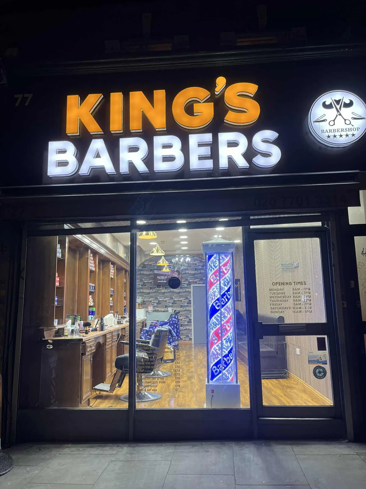 KING'S BARBERS at night: the illuminated amber and white sign, the giant barber pole in the window and the salon glowing behind the glass
