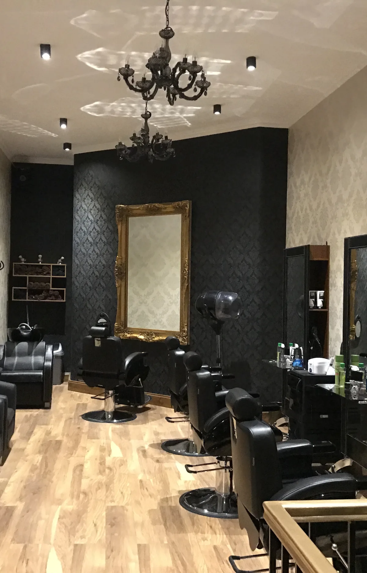 Inside Lalo's Barber Shop: black barber chairs, chandeliers, a gold-framed mirror on a black damask wall and pale wood floors