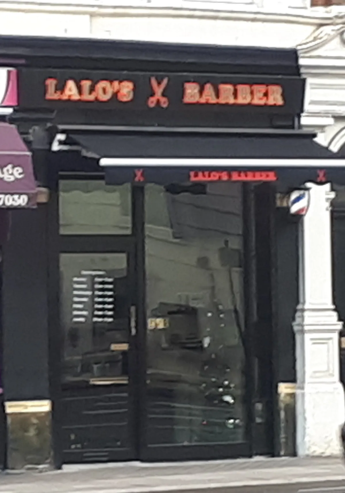 The Lalo's Barber Shop frontage on Vauxhall Bridge Road: black fascia with coral-red lettering, awning and barber pole