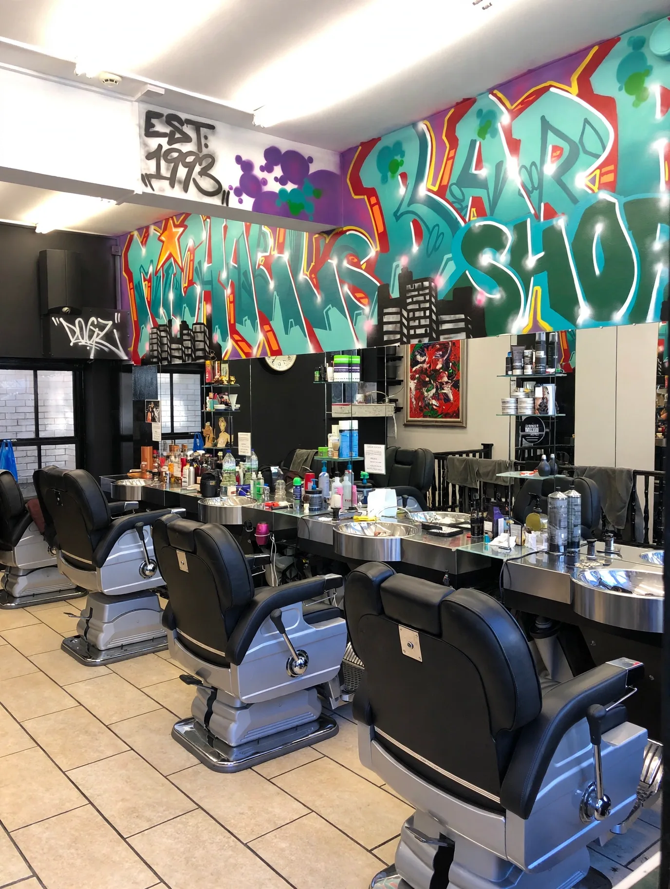 Inside Michael's Barber Shop: black and chrome barber chairs and wash basins beneath a huge colourful graffiti wall reading Michael's Barber Shop, with an EST 1993 tag
