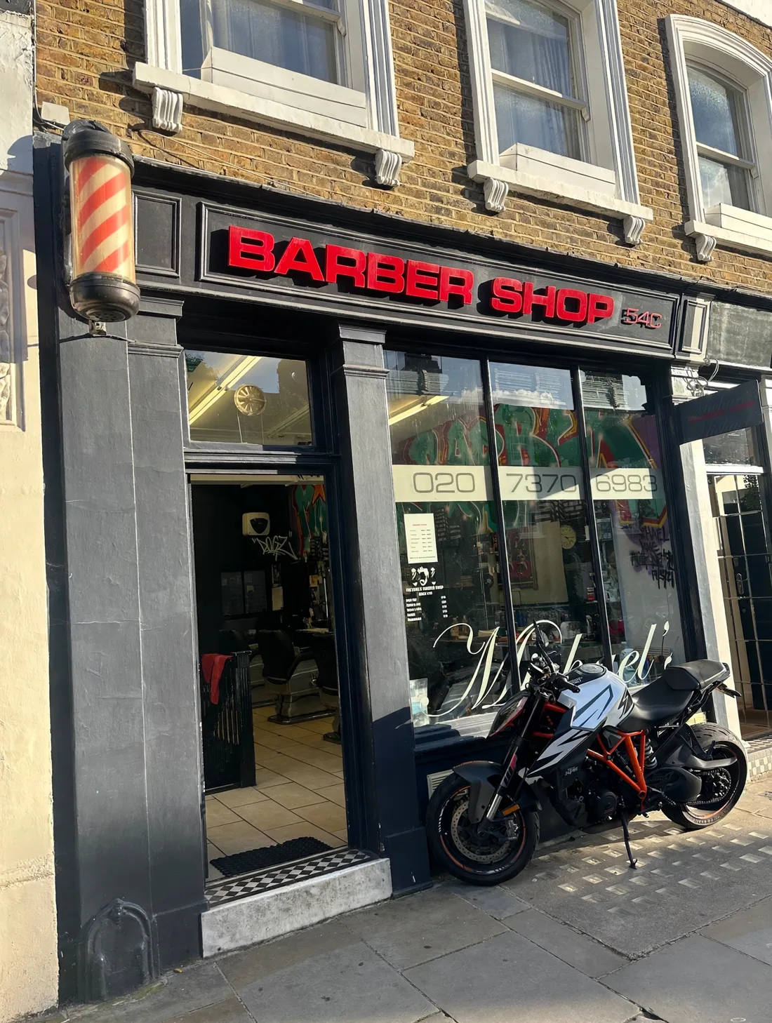Michael's Barber Shop frontage on Kenway Road: black facade with red BARBER SHOP 54C lettering, a barber pole and a motorbike parked outside