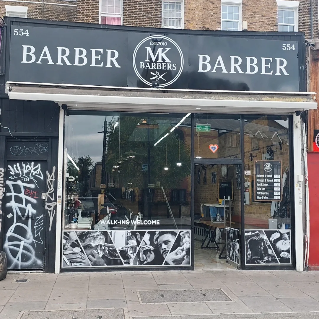 MK Barbers at 554 Kingsland Road: the black fascia with the MK roundel, walk-ins welcome on the window and black-and-white barber artwork decals