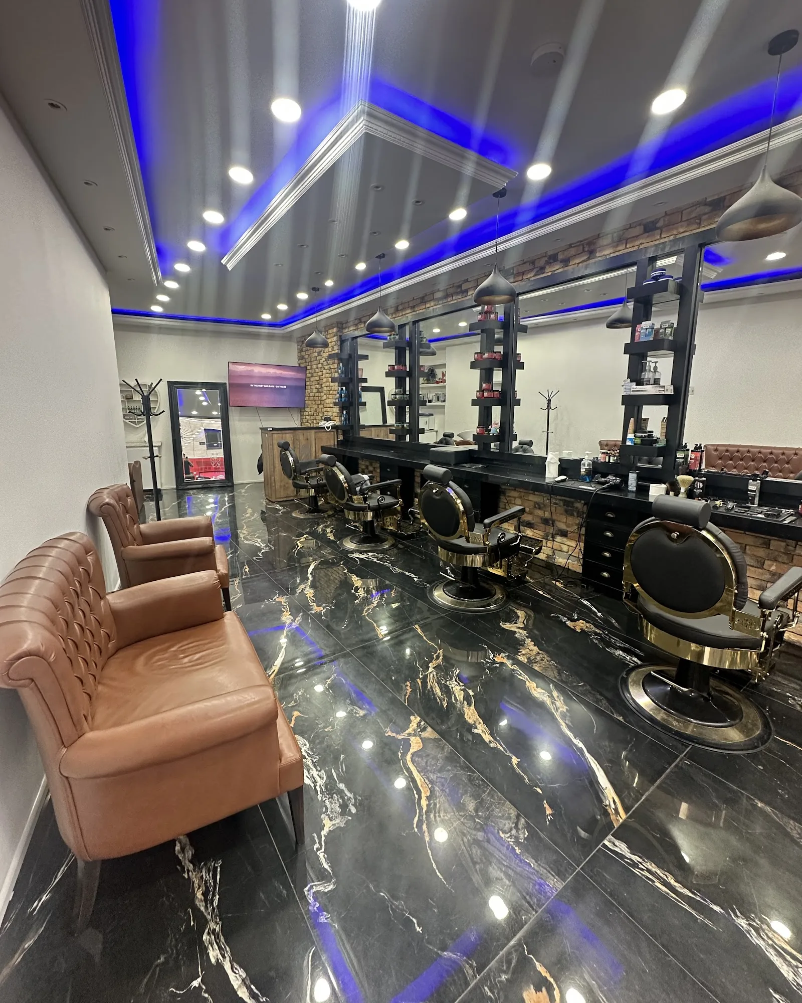 Inside Mr Adam's Barbers: black marble floor, gold-trimmed barber chairs, tan leather waiting sofas and a blue-lit ceiling