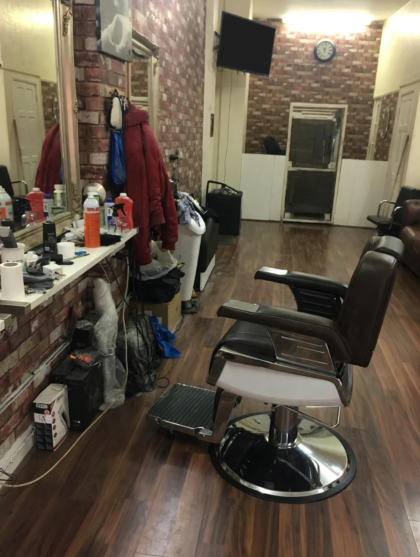 Inside Mr C Barbers: an empty chrome and leather barber chair on a dark wood floor, with exposed brick walls, a mirror counter and a wall clock