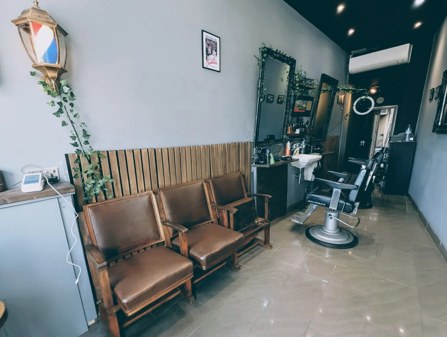 Inside NO.1 Barber Shop: brown leather waiting chairs on a timber slat wall, ornate mirrors, a wash basin and ivy trailing around a barber-pole lantern
