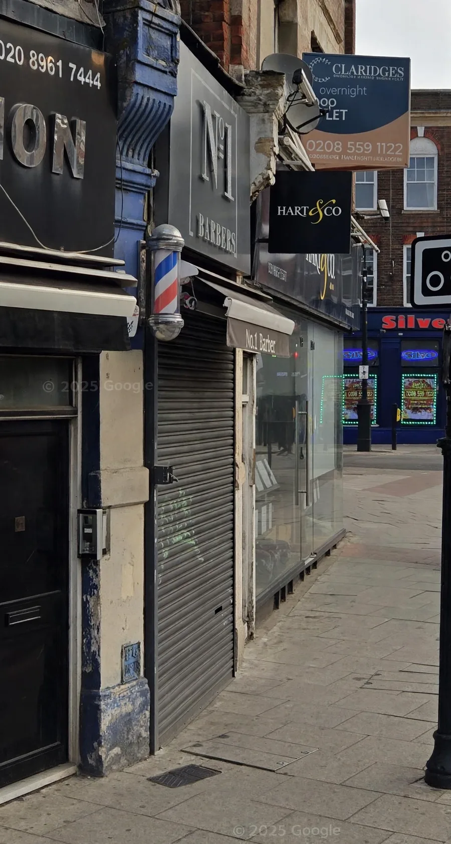 NO.1 Barber Shop on Manor Parade: the grey N°1 BARBERS fascia, the barber pole and the No.1 Barber awning sign, shutters down in this Street View shot