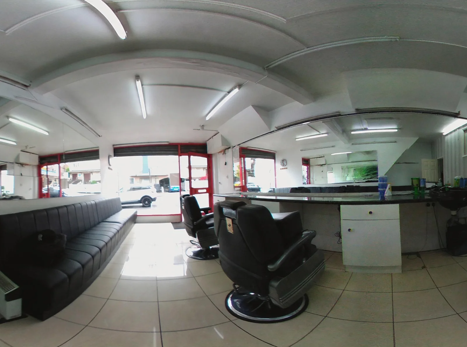 Inside Omar Barber Salon: black barber chairs and a long waiting bench, white counters with mirrors, cream tiles and the red-framed shopfront windows