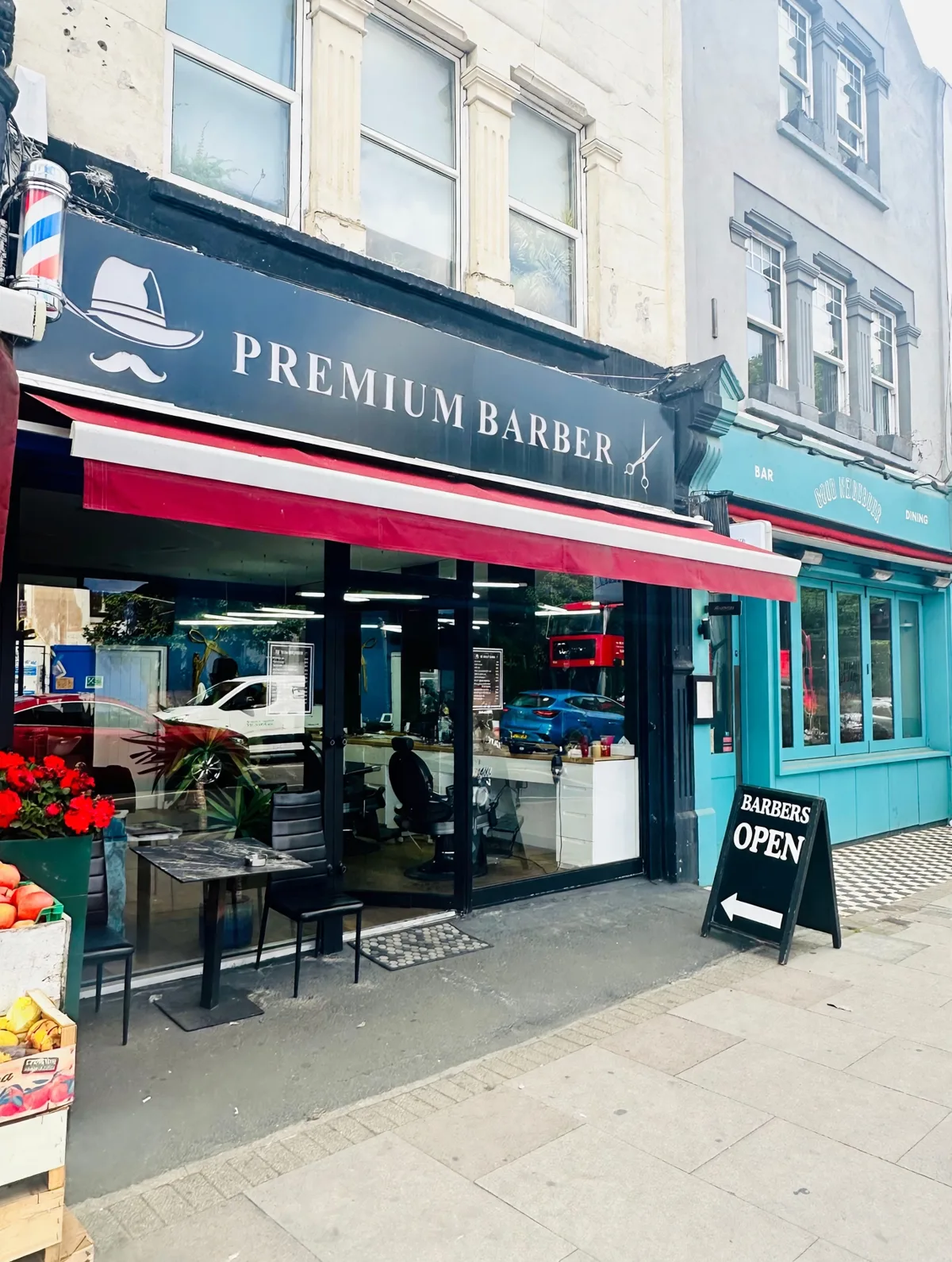 Premium Barber on Tooting High Street: navy fascia with hat-and-moustache logo, red awning and the Barbers Open A-board