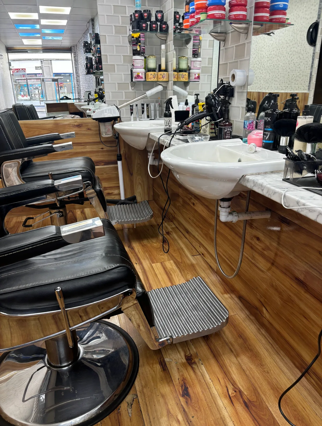 Inside RAK Barbers: timber-clad cutting stations with white ceramic sinks, black leather chairs and a wood floor