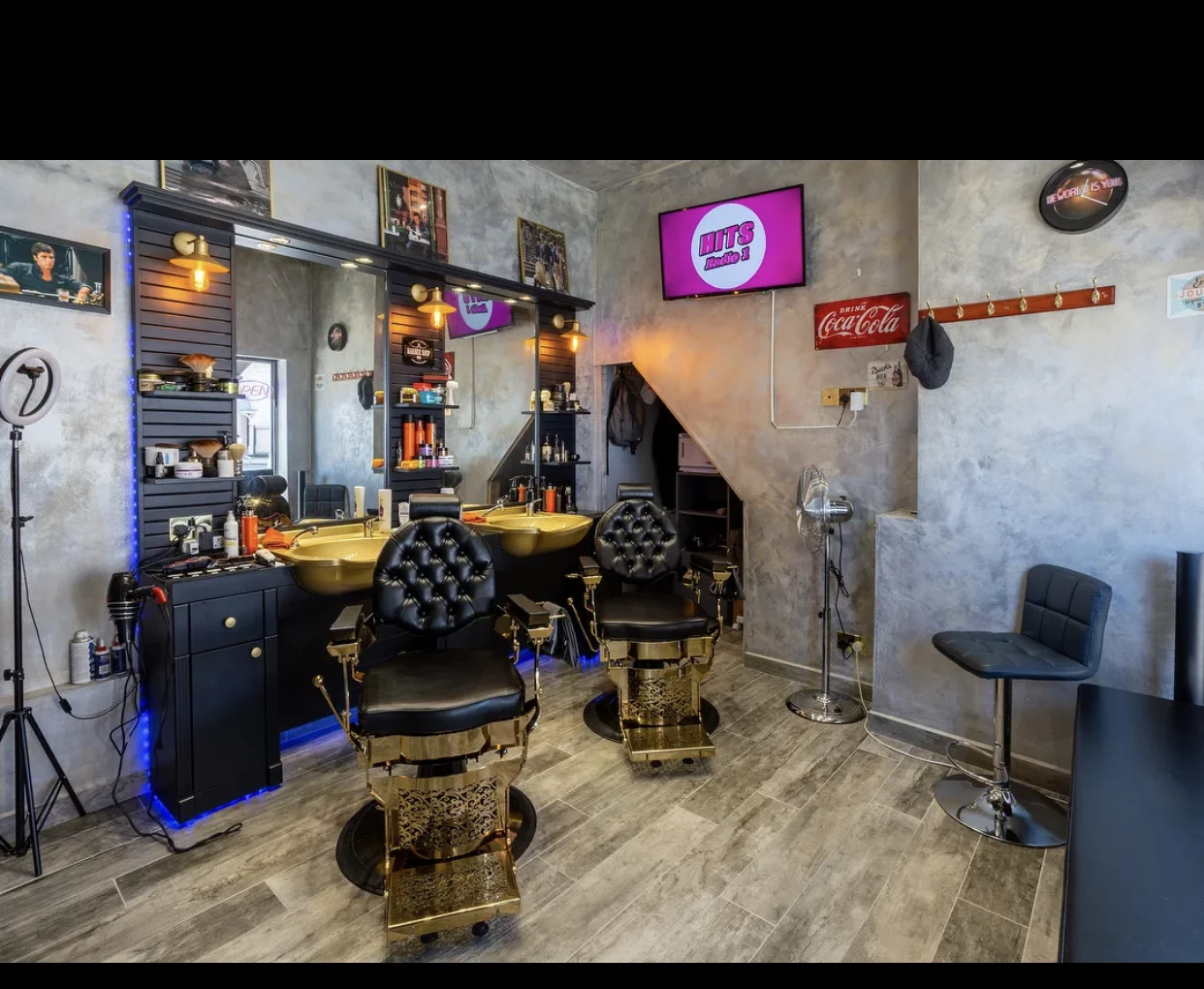 Inside S Barber's: two ornate black-and-gold barber chairs, gold wash basins, dark slatted mirror wall and concrete-textured walls