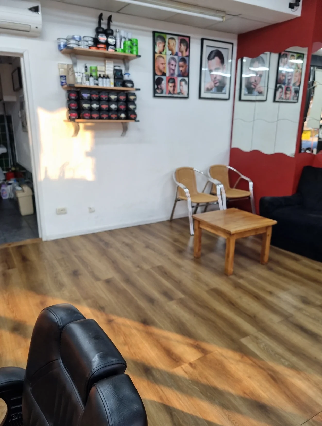 Inside Simon Barbers — shelves of styling products, framed hairstyle posters, a red mirror wall and the waiting corner