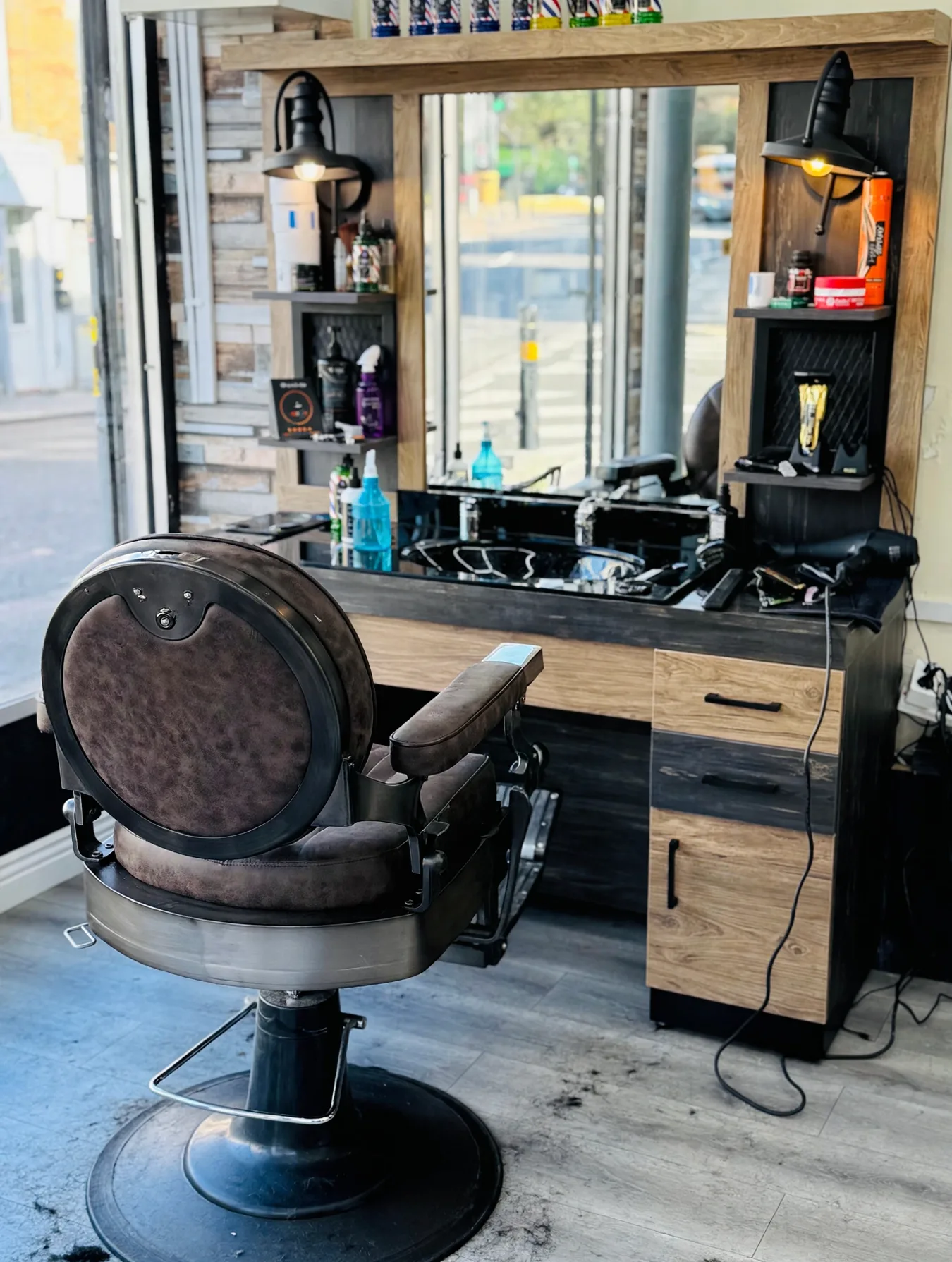 A Style Barbers cutting station: an empty vintage brown barber chair before a rustic timber mirror unit with sink and products