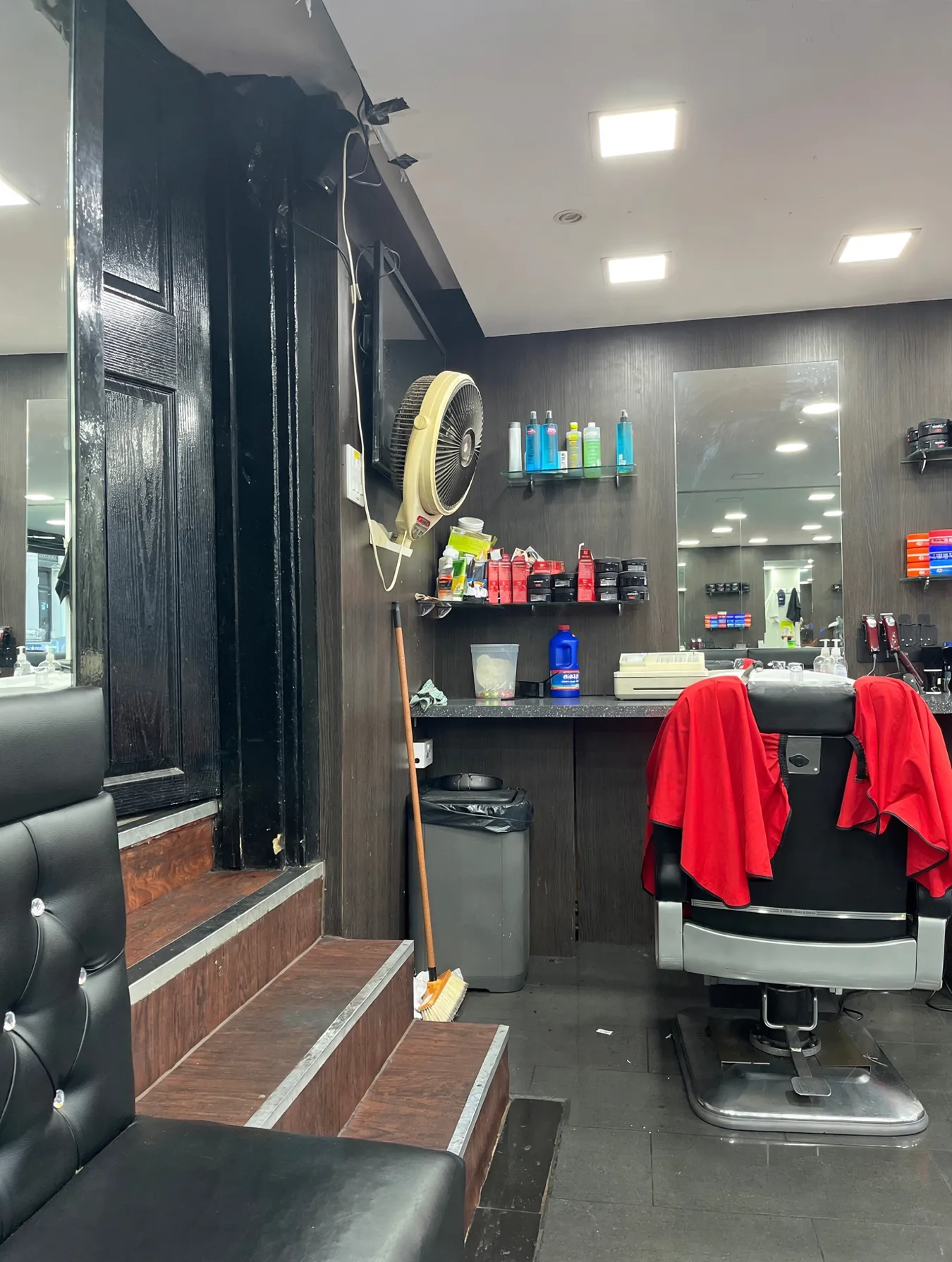 Inside Tanha Habibi Barbers: dark wood panelling, a black leather waiting bench, product shelves and a barber chair with red towels