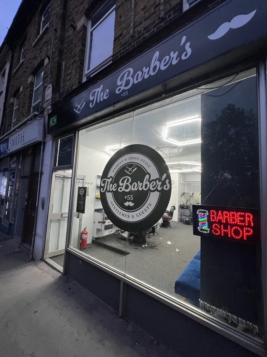 The Barber's +55 shopfront at dusk with its circular window logo and LED barber sign