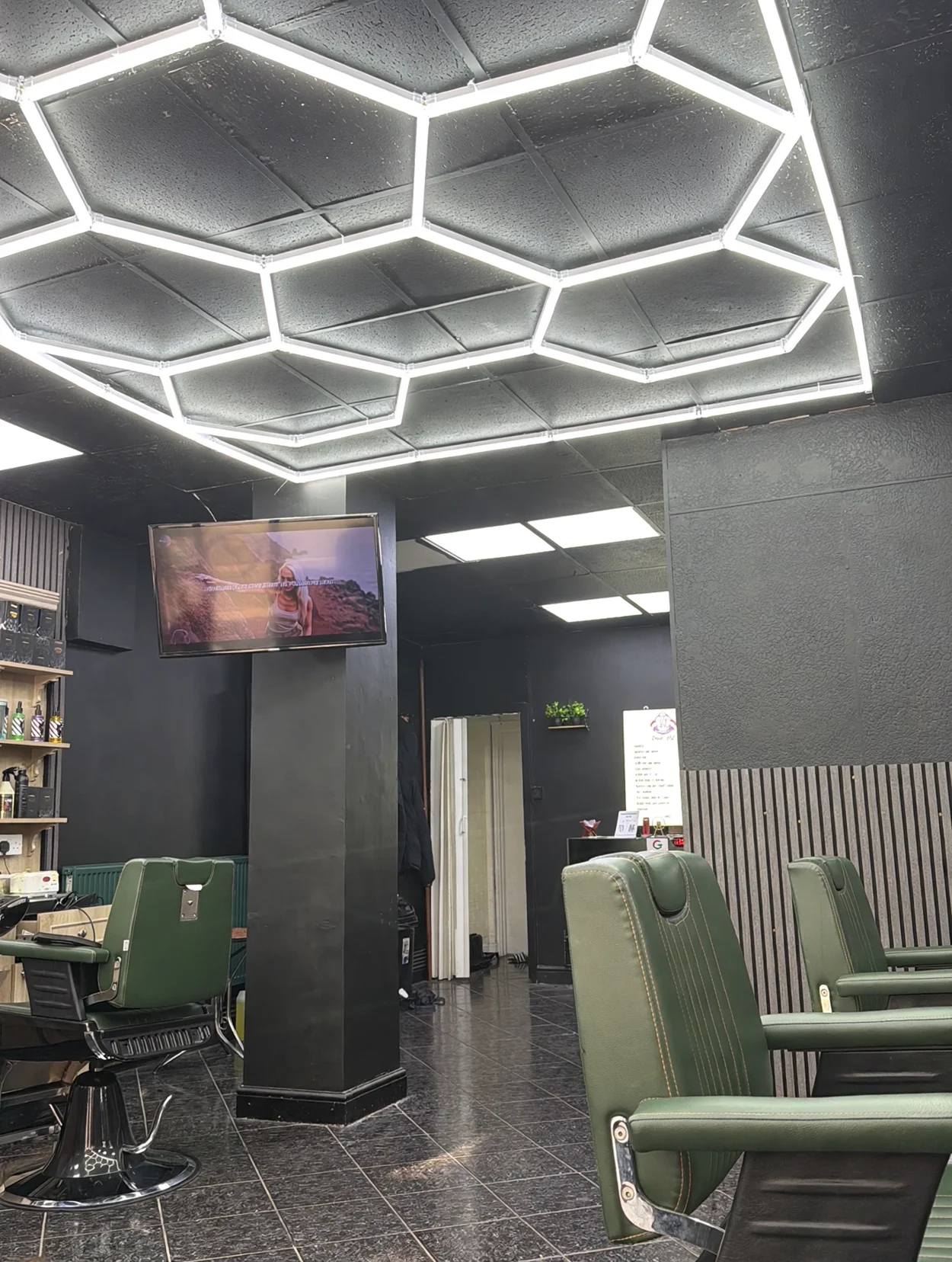 Inside The Palace Barber — green leather chairs under a honeycomb LED ceiling, dark walls and a pillar TV