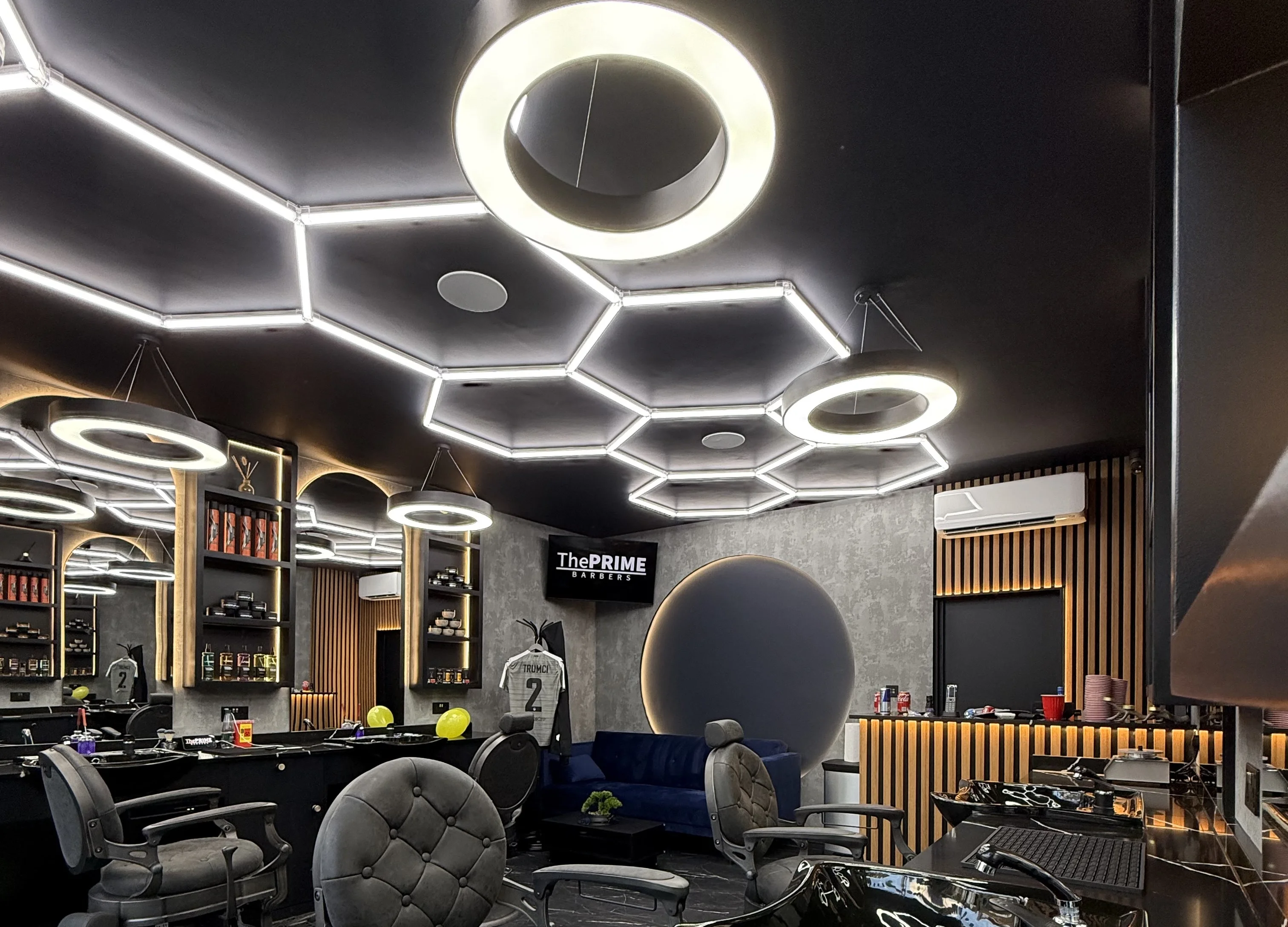 Inside The Prime Barbers: hexagonal LED ceiling lights, ring pendants, black marble counters and floor, tufted chairs, a moon-disc wall feature and the blue velvet sofa