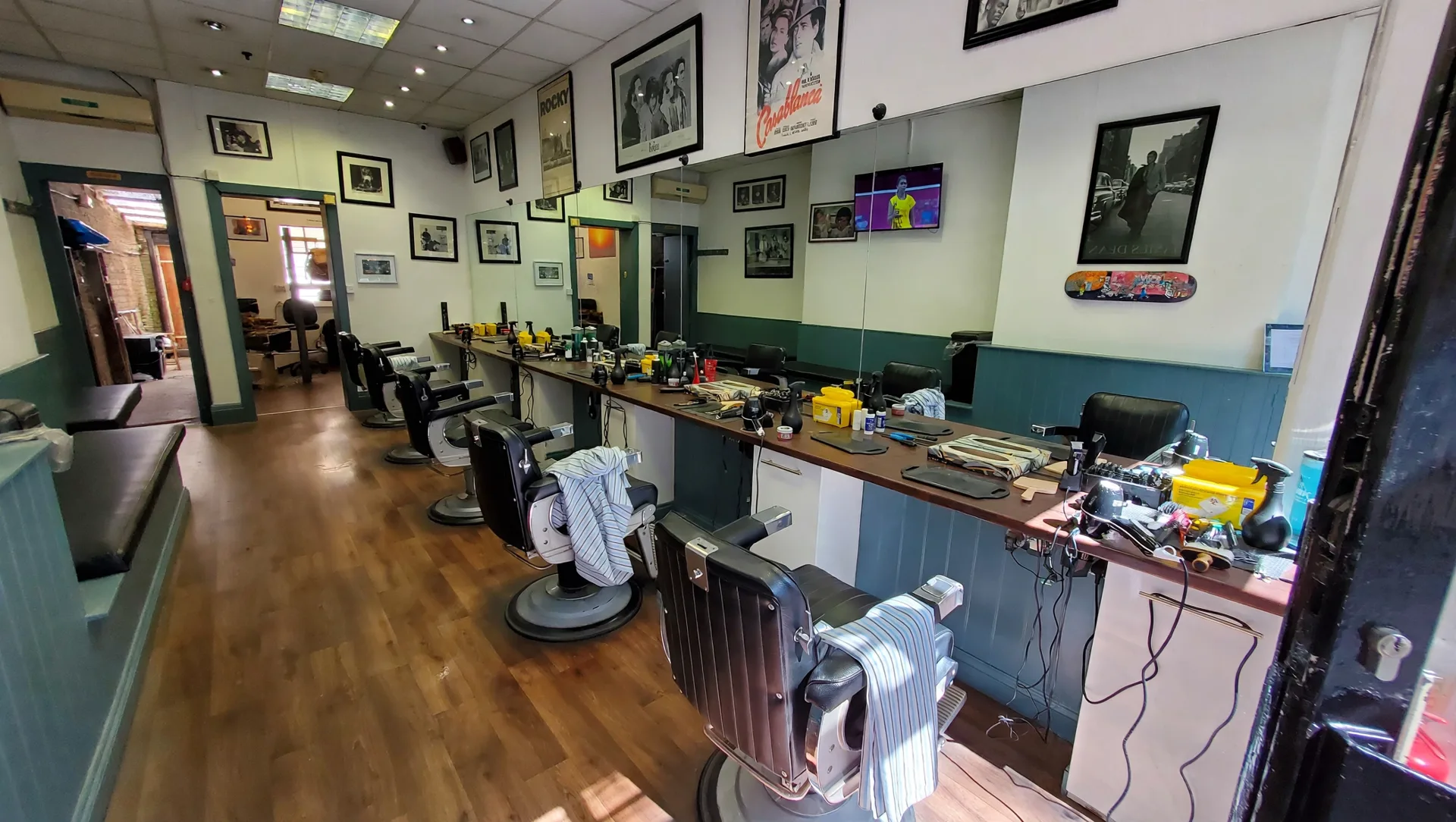 Inside Toff's Barber Shop: a long traditional salon with vintage barber chairs, a tool-lined wooden counter, wood floors and framed film posters