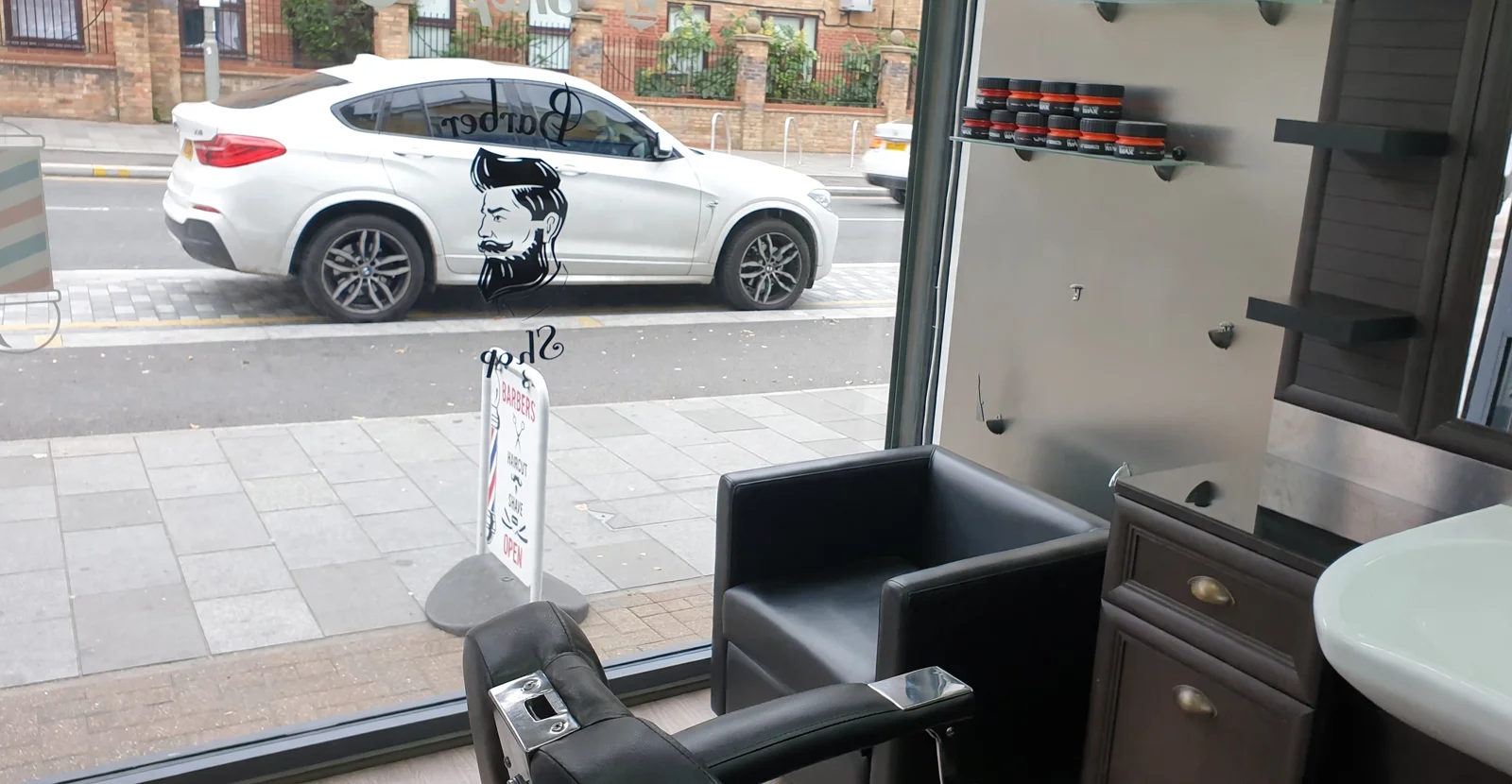 Inside VIP Style Barbers: dark wood cabinets, a white sink, product shelves and the big front window with the shop's bearded-man logo decal looking onto Forest Road