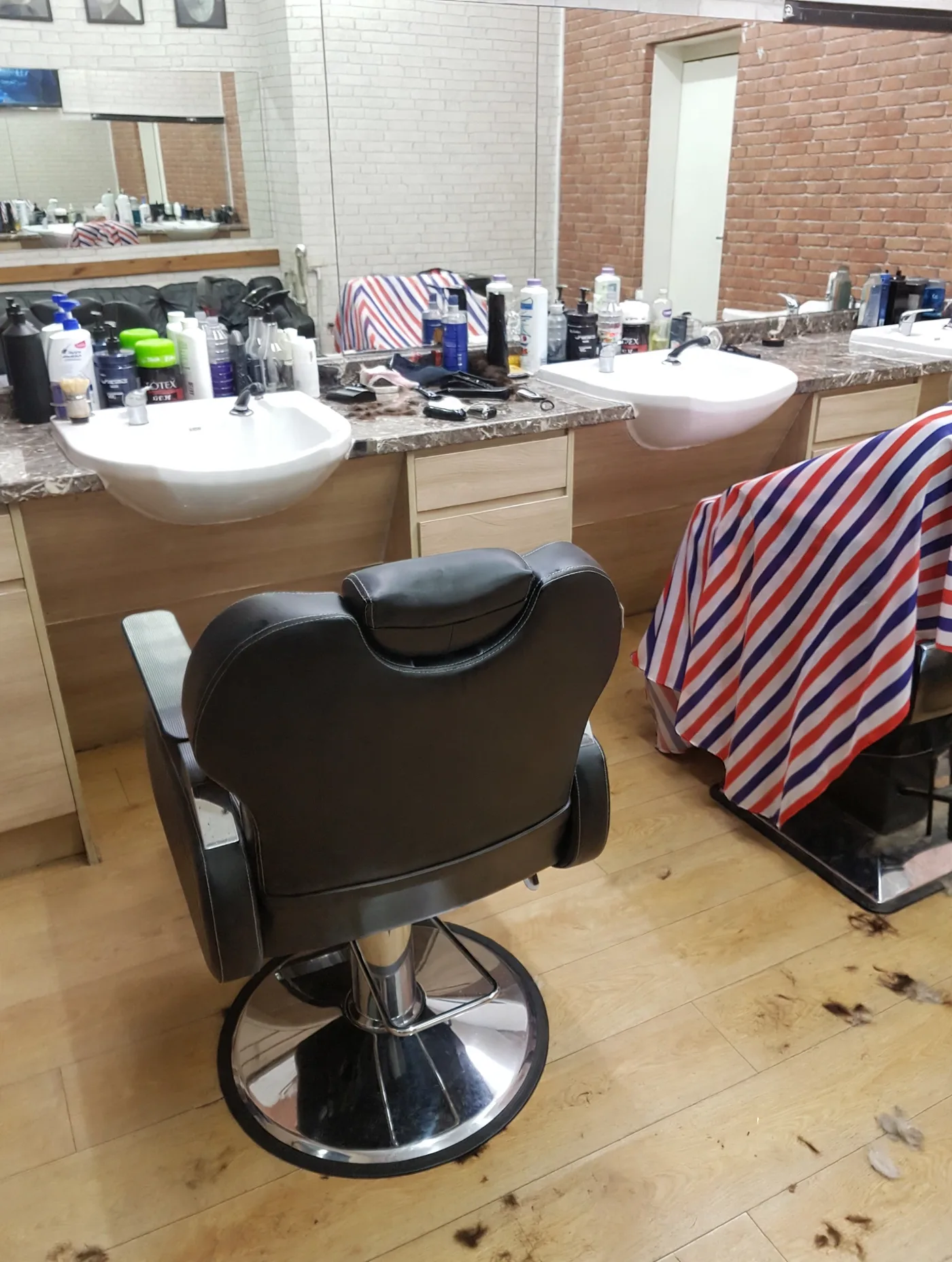Inside V&K Barbers: an empty black barber chair between two white washbasins, with product bottles, mirrors and brick walls