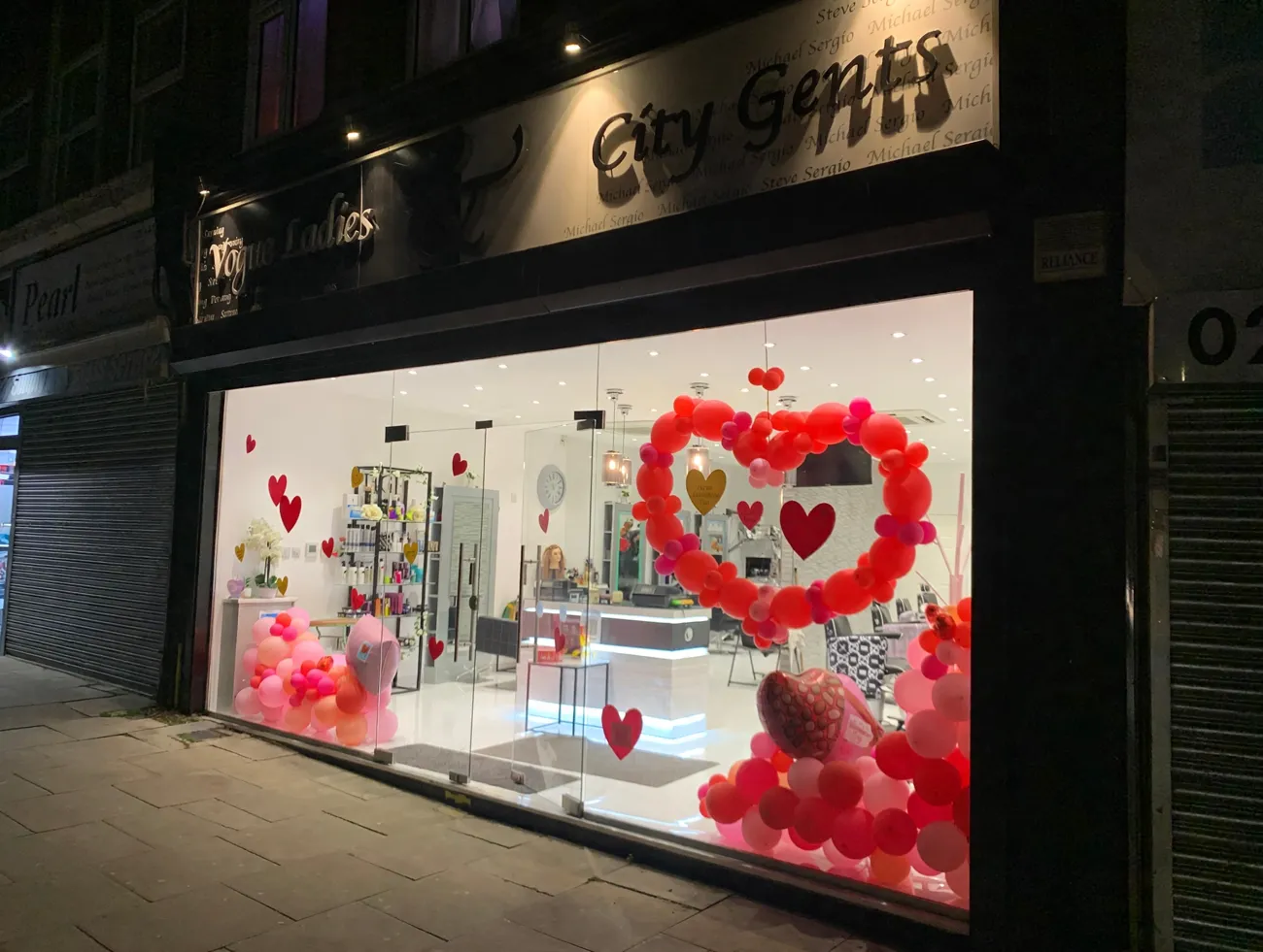 Vogue Ladies and City Gents shopfront at night with its balloon arch