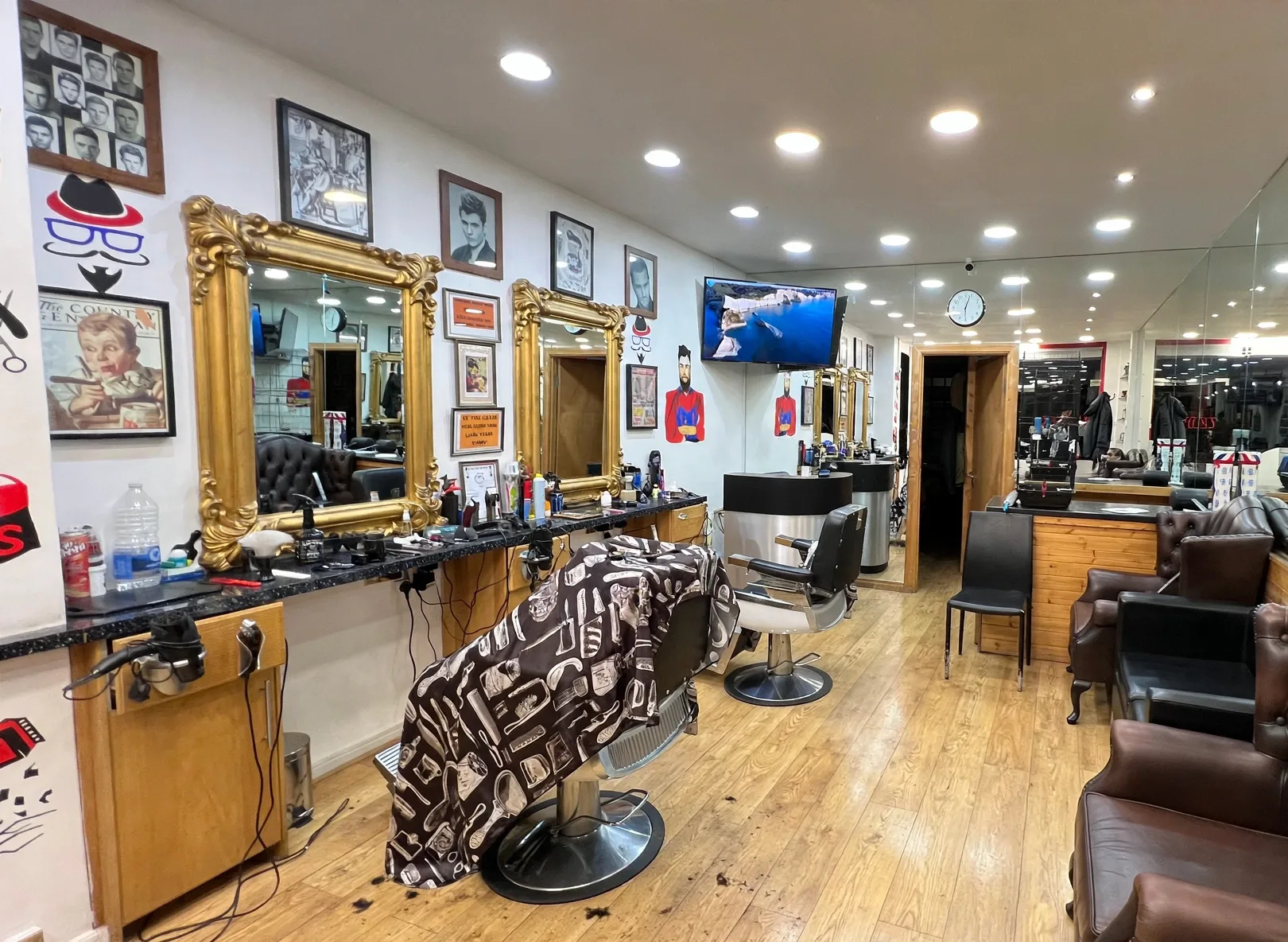 Inside Zidane Barbers: ornate gold-framed mirrors, black counters with tools, wood floors and brown leather waiting chairs